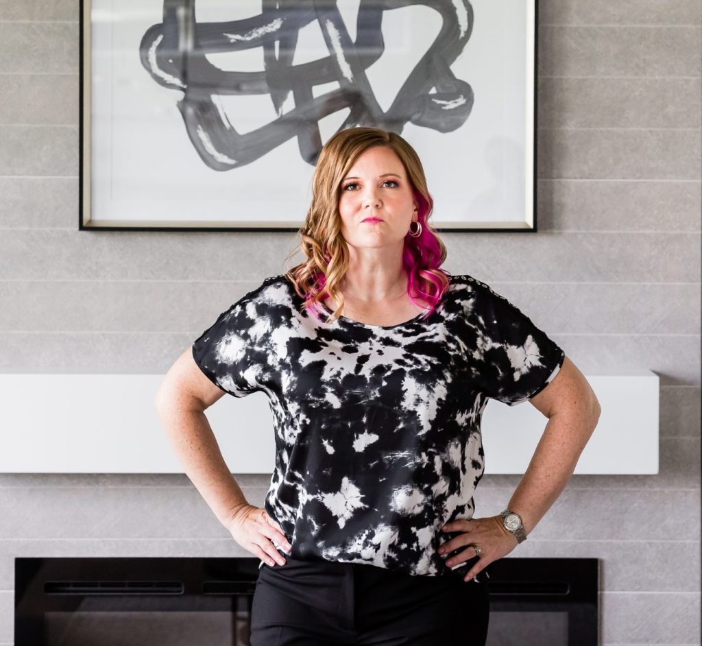 Pamela, a tech VA and systems strategist for women entrepreneurs, standing confidently in front of a fireplace in a modern home office.